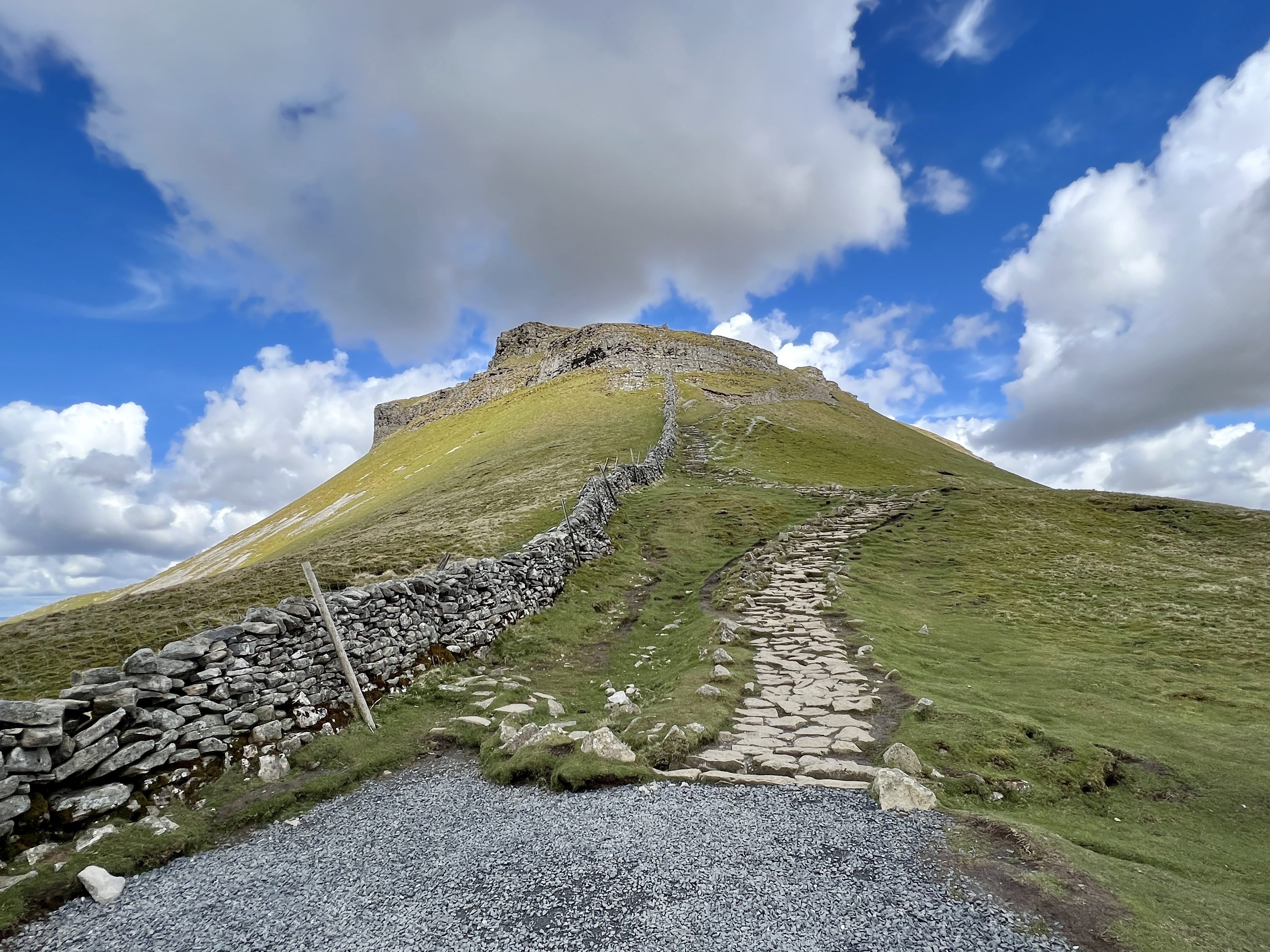 Pen-y-Ghent is one of the Yorkshire Three Peaks, standing at 694 meters (2,277 feet), it the lowest of the three. Its distinctive shape and dramatic, tiered appearance makes it the most visually striking. 
As we were looking for a longer walk, without doing the three peaks; we started in the village of Austwick. Resulting in a 16 miles circular route combining wild limestone country, green fields with lambs, scars and caves (including Hull Pot) and a more solitary approach compared to the classic Horton circuit.